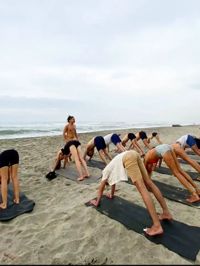 Clase de yoga en la playa, con el grupo en postura del perro boca abajo